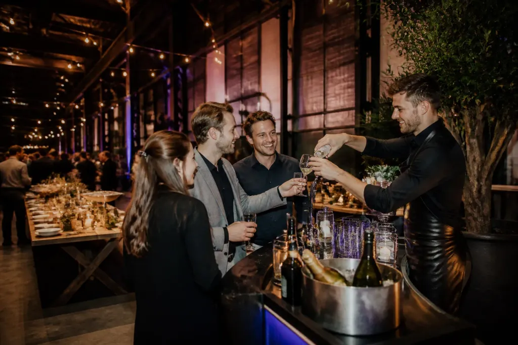 industrieel ingerichte feestlocatie met mobiele cateringbar en collega’s die proosten tijdens bedrijfsfeest