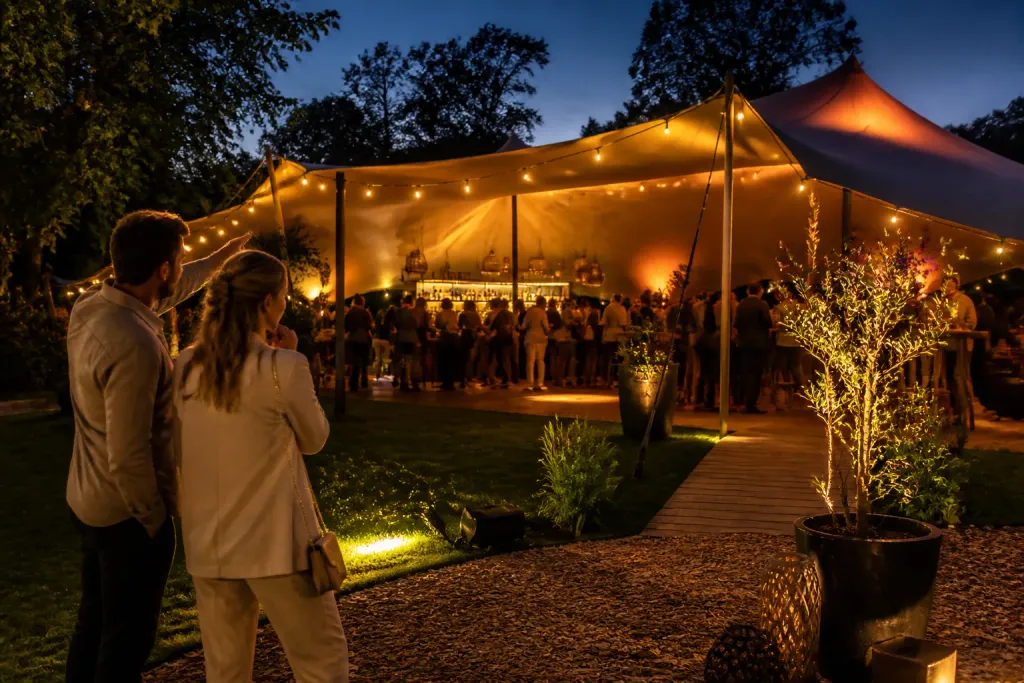 stel bekijkt een warme stretchtent in een avondtuin met feestende gasten en bar