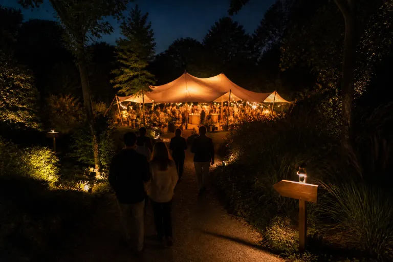 verlichte stretchtent in een avondtuin die als baken dient voor gasten die via een tuinpad naar de bar lopen